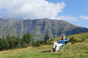 Beautiful blonde sitting on a sun lounger in the mountains. Concept: mountain tourism and mountain travel.