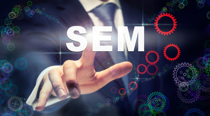 A businessman pressing a SEM business concept on a graphical display of cogs
