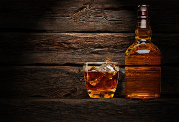 Bottle and glass of whiskey on wooden table or desk background