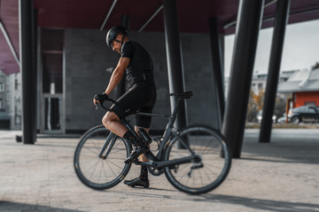 Sportsman riding bike next to modern building inside urban bridge.