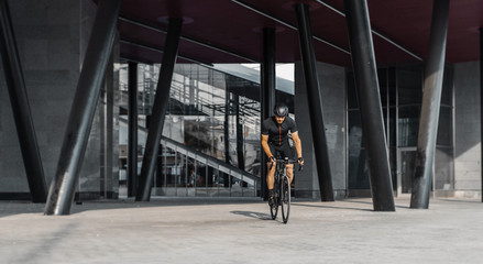 Sportsman riding bike next to modern building inside urban bridge.