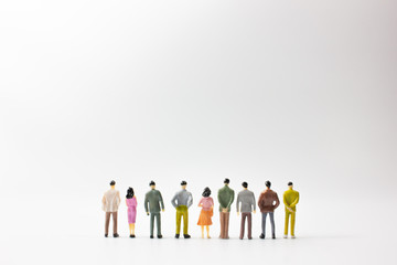 A group of miniature business people stand on white background back view.