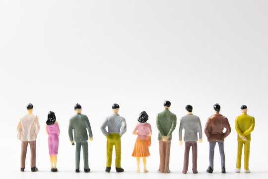 A group of miniature business people stand on white background back view.