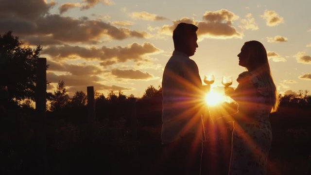 Romantic multi-ethnic couple drinking wine at sunset. They stand near the vineyard. Honeymoon and travel concept