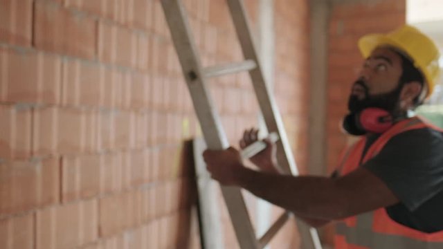 Confident people working in construction site. Portrait of happy hispanic man at work in new house inside apartment building. Professional latino worker using ladder and smiling at camera. Slow motion