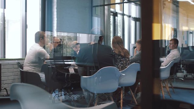 Meeting of young positive businessmen, discussion of the details of the business project. Young people are in a beautiful glass office.