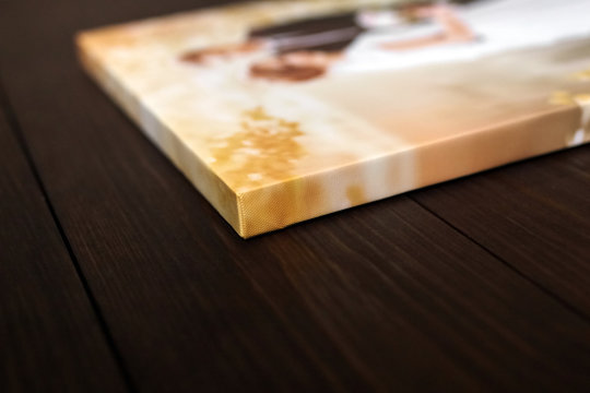 Sample of photography with gallery stretch on a wooden frame. Printed wedding photo on canvas lying on wooden table. Lateral side closeup. Selective focus