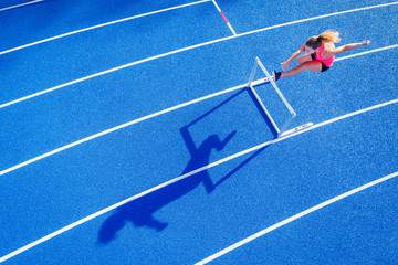 Top view of female runner crossing hurdle on tartan track