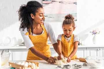 attractive african american mother and adorable daughter kneading dough in kitchen - obrazy, fototapety, plakaty