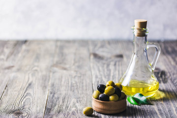 Obraz premium Extra vergin olive oil in glass jar, marinated olives in wooden bowl on rustic background. Selective focus, space for text.