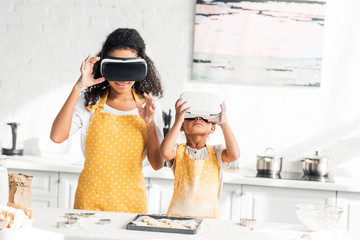 african american mother and daughter preparing dough in virtual reality headsets in kitchen