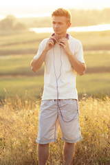 teenager in headphones listening to music on nature, young man resting in summer field, concept sport and music