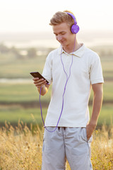 teenager in headphones listening to music on nature, young blond man relaxing in summer field