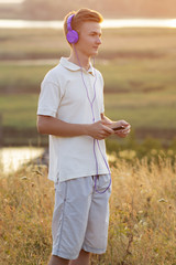 teenager in headphones listening to music on nature, young man is relaxing and enjoying of a beautiful summer landscape,concept sport and music