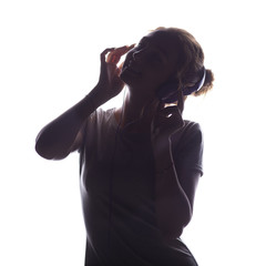 silhouette of a girl listening to music in headphones, young woman relaxing on a white isolated background, concept of hobby and leisure