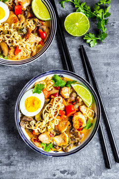 Ramen soup with egg, noodles, chicken meat, paprika, mushroom, spring onion, lime and coriander