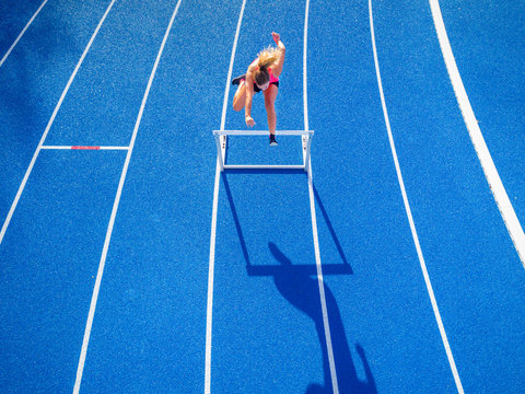 Top view of female runner crossing hurdle on tartan track