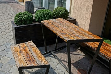 brown wooden table and benches on the sidewalk with pot with greens on the walls