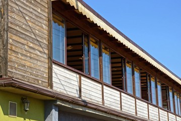 large wooden brown balcony porch with windows against a blue sky