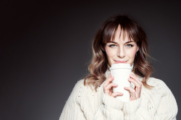 Beautiful woman with long hair wearing red hat and sweater holds shows paper disposable coffee cup. Space for design template layout mock-up.