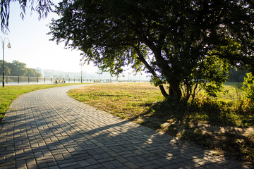Ukrainian park outdoor paved curved cycle road along river shore in city waterfront district under tree shadow in morning fresh clear weather time