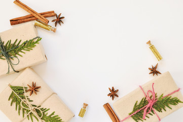 Cozy holiday background in warm, trendy colorsand white. Christmas composition of spruce branches, gift, cinnamon, anise and confetti in small jars. Flatlay, top view