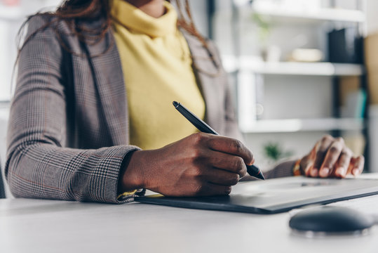 midsection of african american designer using graphic tablet at desk in modern office