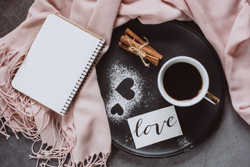 Valentines day. Cup of coffee, notebook, scarf, cinnamon and heart on gray table from above in flat lay style.