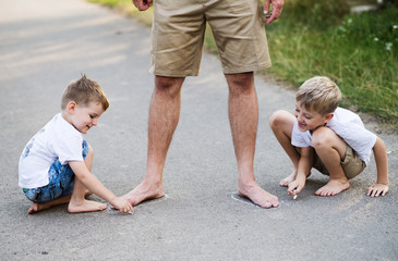 Fototapeta premium Two small sons playing with father on a road in park on a summer day.