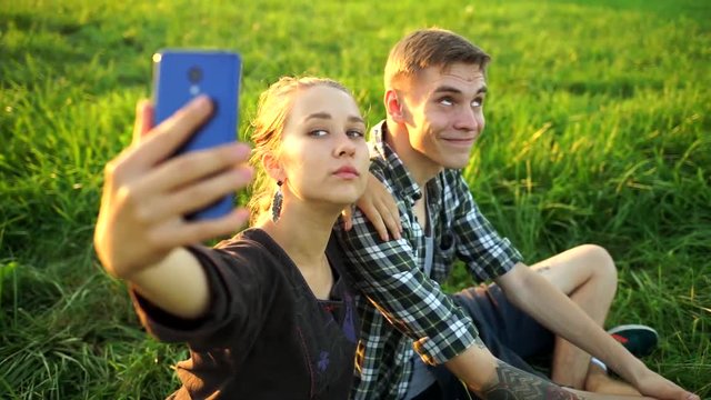 A guy and a girl sit on the grass and take selfies. Couple on a picnic doing a selfie. People in love look at the phone and smile.Friends fooling around in front of the camera.The lovers posing.