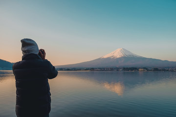 man traveler standing and taking photo Beautiful Mount Fuji with snow capped in the morning sunrise at Lake kawaguchiko, Japan. landmark and popular for tourist attractions. travel concept