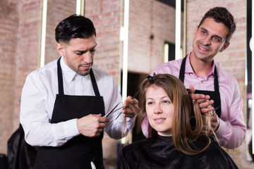 Two hairdressers making hairstyle for female client