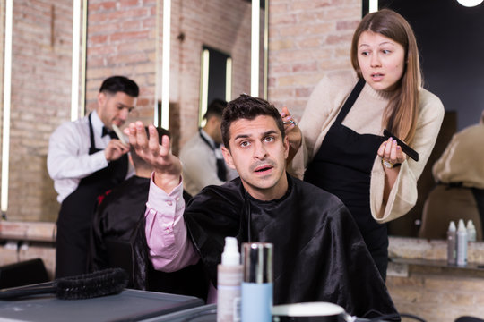 Shocked man with apologetic hairdresser at barbershop
