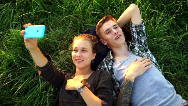 A guy and a girl lie on the grass and take selfies. Couple on a picnic doing a selfie. People in love look at the phone and smile.Friends fooling around in front of the camera.The lovers posing.