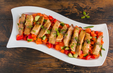Tilapia fish fillet roasted in olive oil and served with fresh vegetable salad in white dish on wooden rustic table, top view