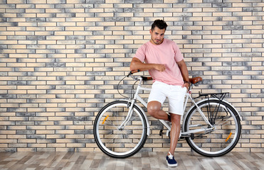 Fototapeta premium Handsome young hipster man with bicycle near brick wall