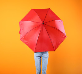 Woman hiding behind red umbrella on color background