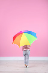 Little girl with rainbow umbrella near color wall. Space for text