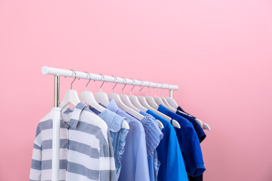 Rack with bright clothes on color background
