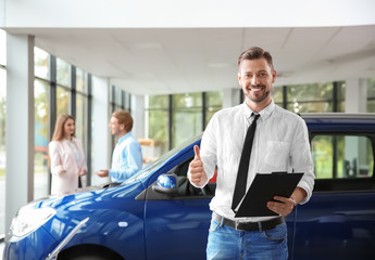 Salesman with clipboard near new car in modern auto dealership