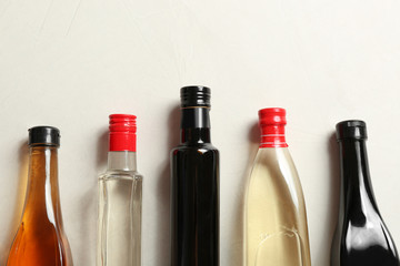 Flat lay composition with different kinds of vinegar in bottles and space for text on light background
