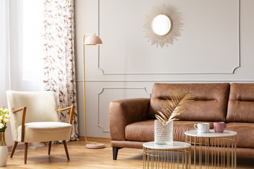 Real photo of a warm living room interior with a leather sofa, armchair, lamp and coffee tables...