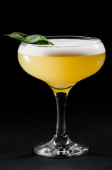 Beautiful yellow cocktail with white froth decorated with mint in a glass chalet isolated against a black background. close-up. dark background. photo series