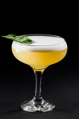 Beautiful yellow cocktail with white froth decorated with mint in a glass chalet isolated against a black background. close-up. dark background. photo series