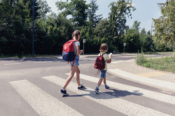 Fototapeta premium Girl and boy with backpacks walking through pedestrian crossing to the school