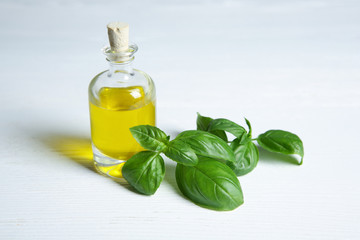 Glass bottle with oil and basil leaves on light table