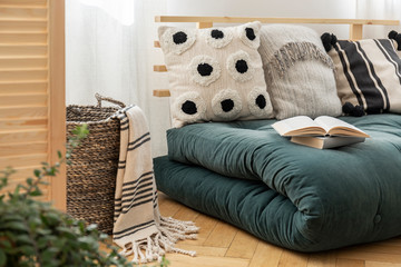 Books on scandinavian futon with pillows in elegant bedroom interior, real photo
