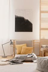 Abstract painting on the white wall of japanese inspired bedroom design with beige futon and yellow pillows