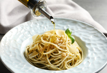 Dressing delicious basil pesto pasta with olive oil, closeup