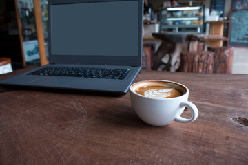Close up of Cup of hot latte art coffee with laptop computer on wooden table, work with coffee concept picture foe business background